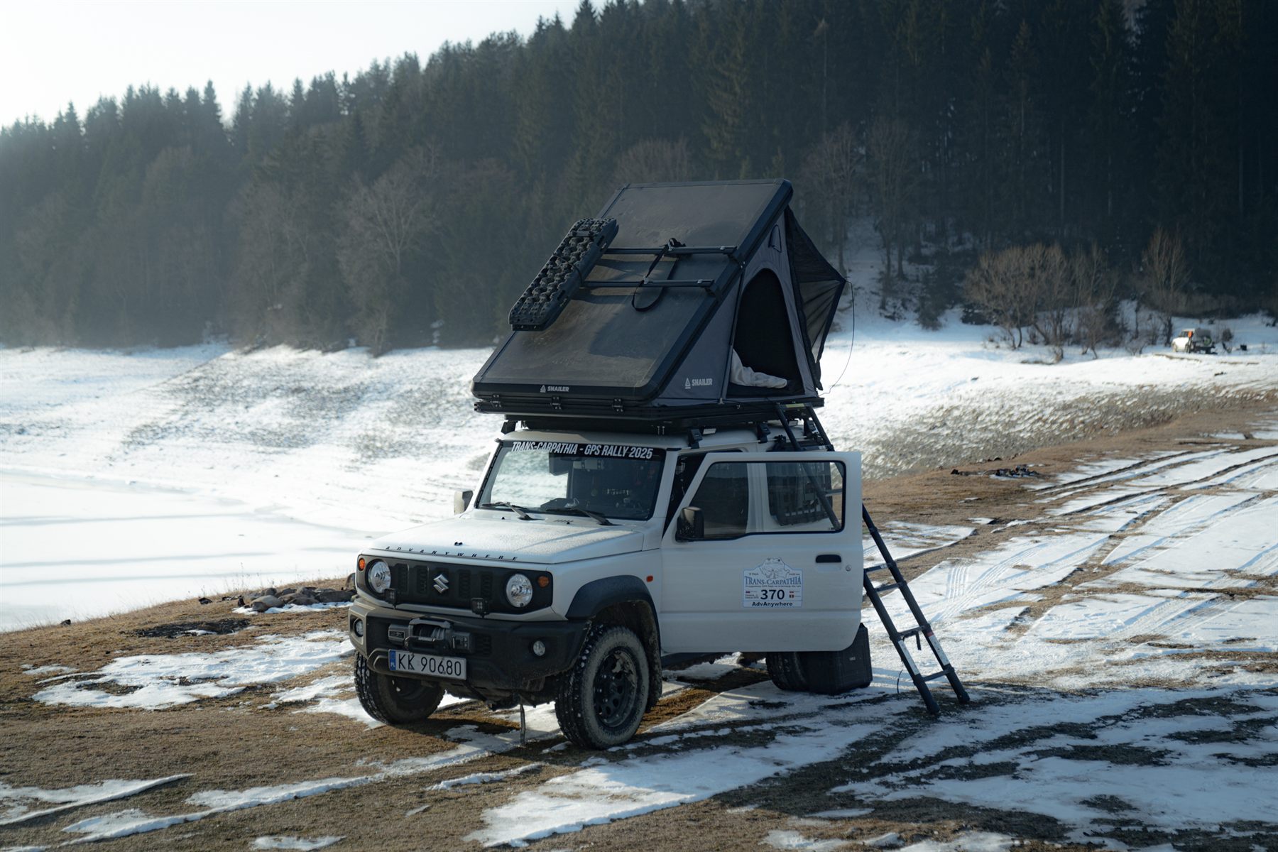 Voiture avec tente de toit stationnée sur un terrain enneigé hors route près d’un lac gelé